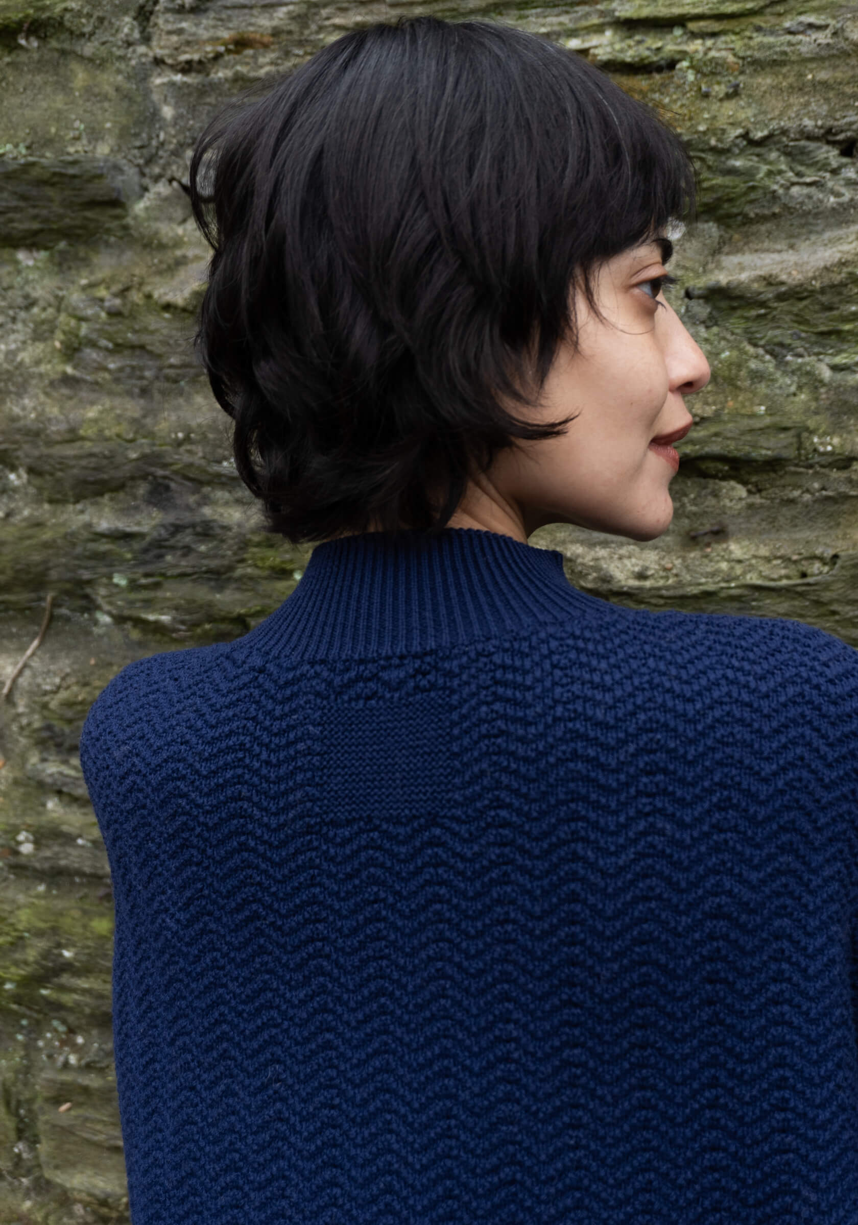 Person wearing a blue knitted sweater against a stone wall.