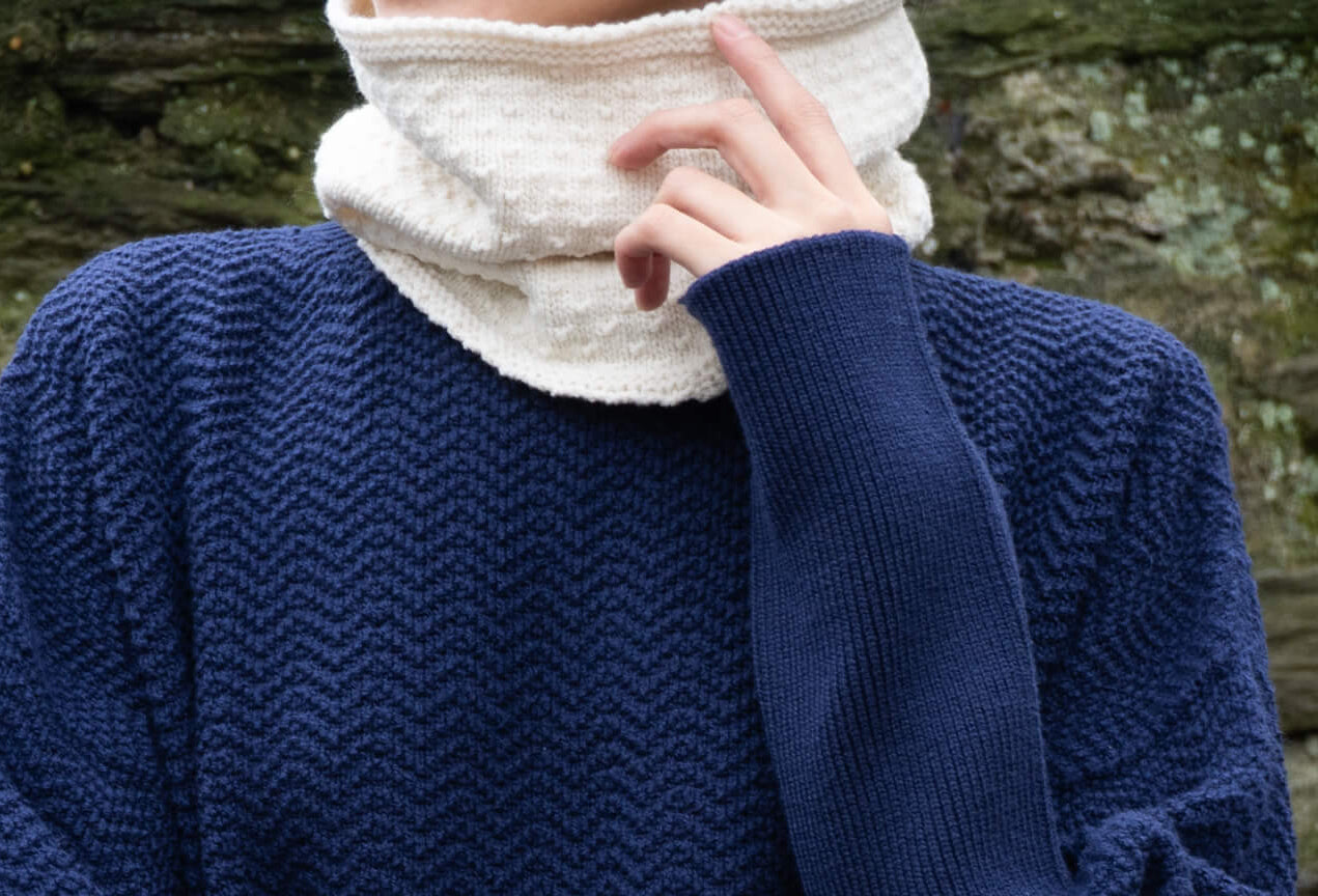 Person wearing a navy blue knitted sweater against a stone wall.