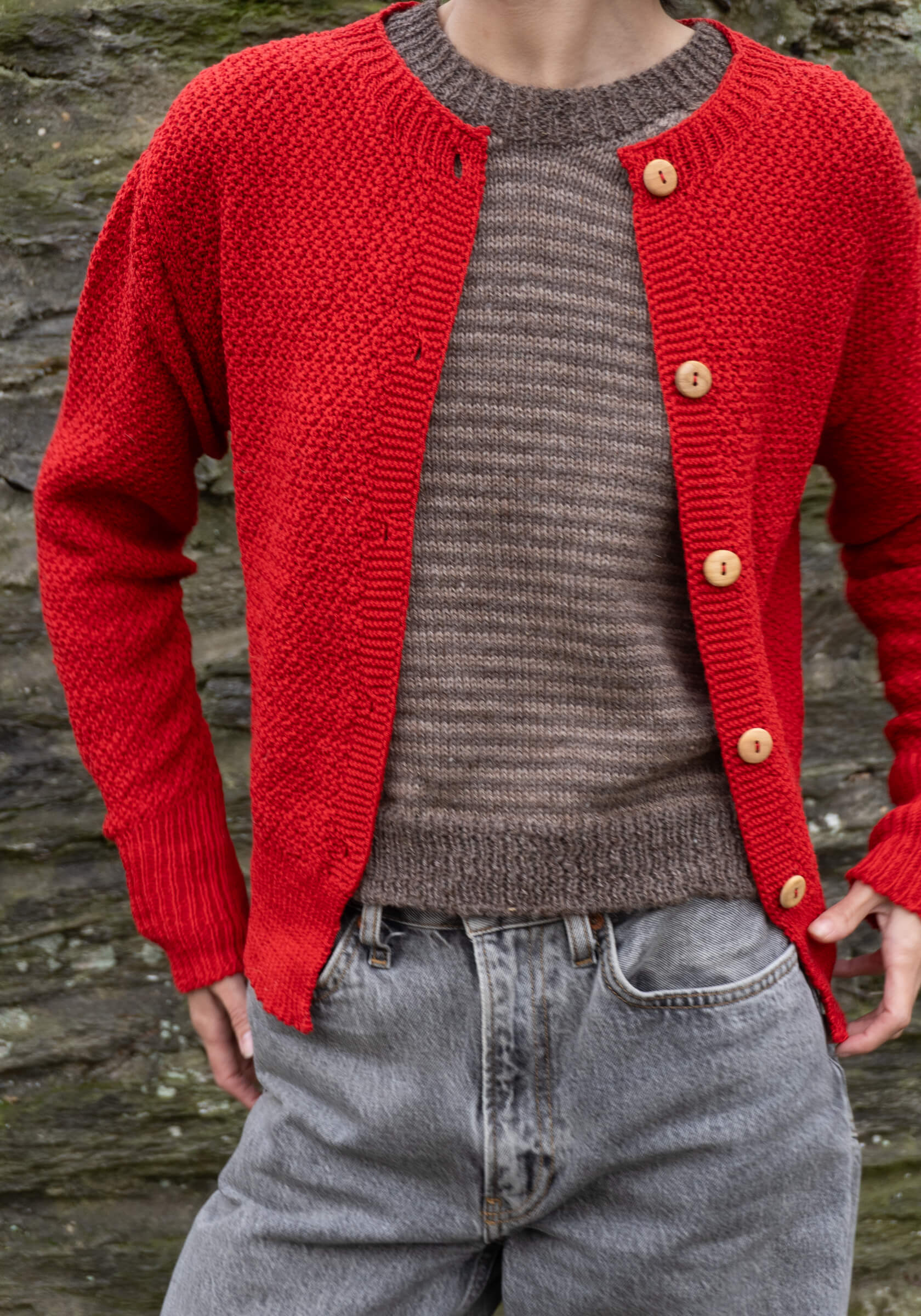 Red knitted cardigan over a gray sweater with a stone wall background