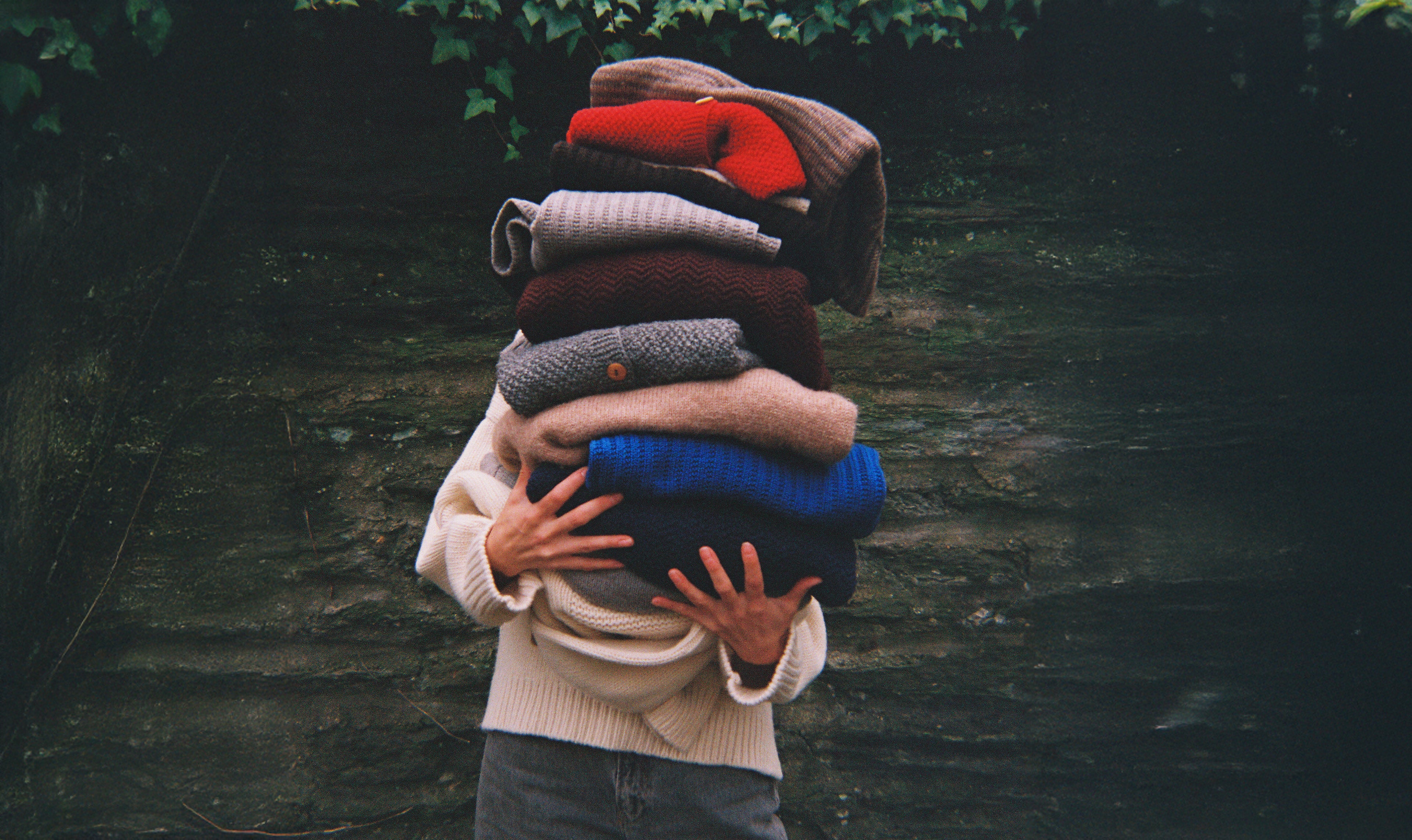 Person holding a stack of colorful sweaters against a dark background